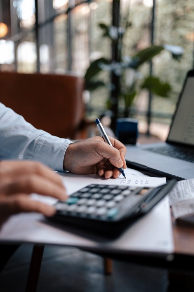 pexels photo 16282306 A person calculating finances with a calculator and pen on a desk indoors.
